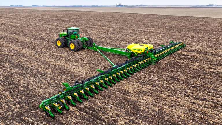 Aerial view of a large green tractor pulling a massive 48-row seed planter across a wide, tilled agricultural field.