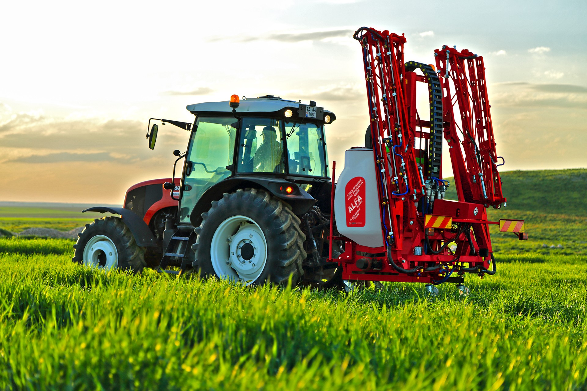 A modern tractor pulling a boom sprayer applying fertilizer across a large agricultural farming field.