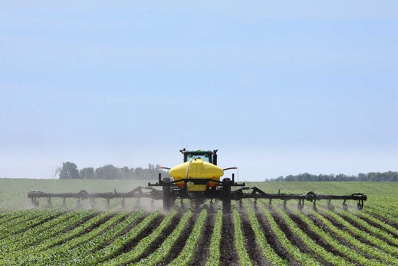Tractor using a row-crop fertilizer applicator across a planted field.