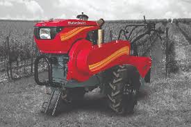 A red power tiller parked in a cultivated agricultural field.