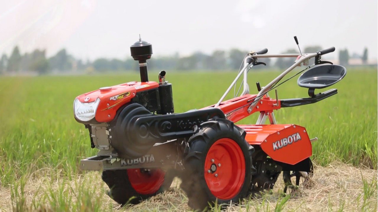 A red power tiller with an operator seat attachment, sitting in a green agricultural field.