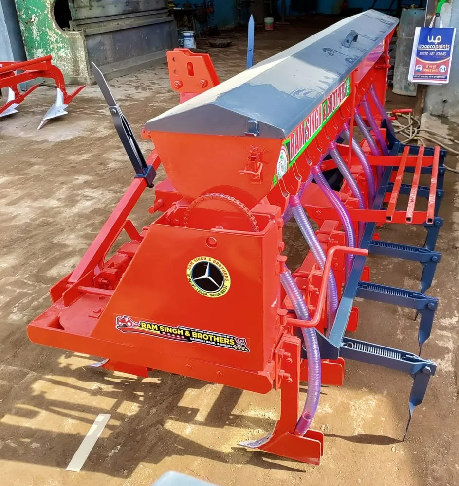 Red seed drill machine with seed tubes and furrow openers for accurate crop planting.