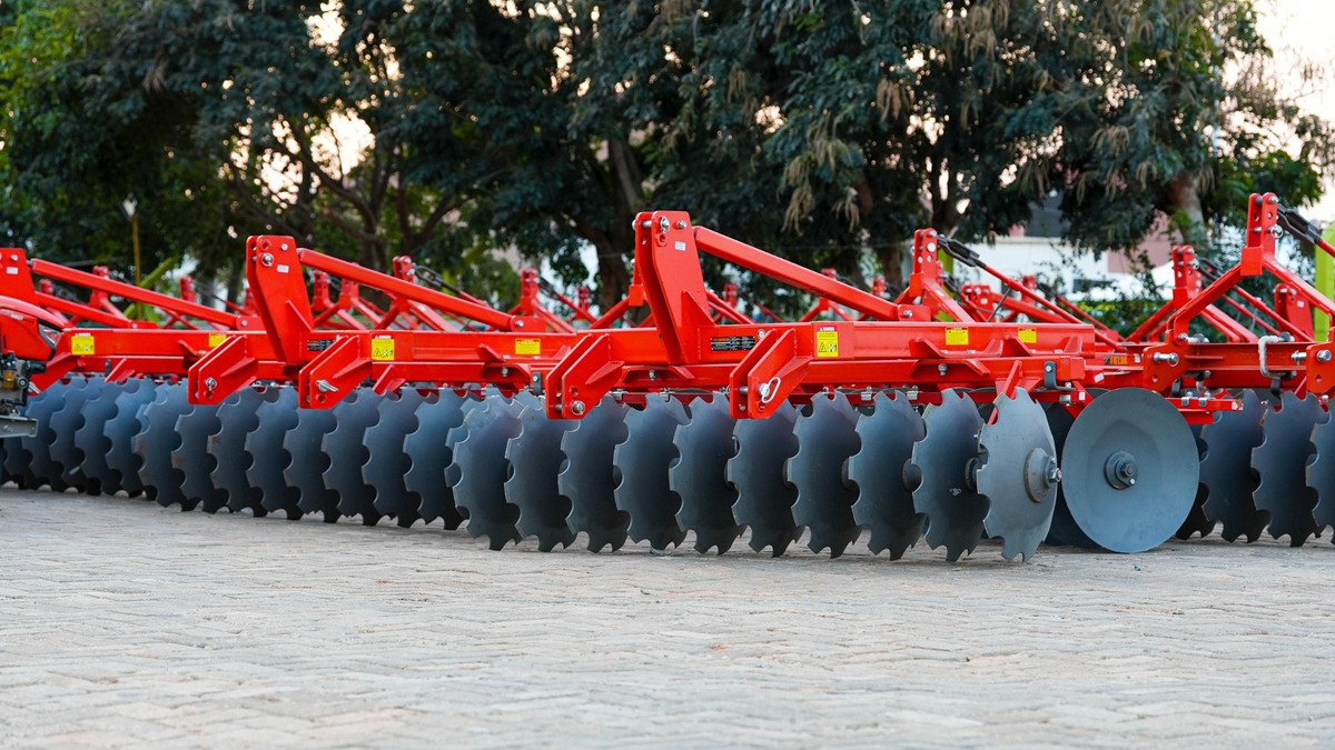 Red disc harrow with rows of black steel blades, used to break up soil and prepare a seedbed.