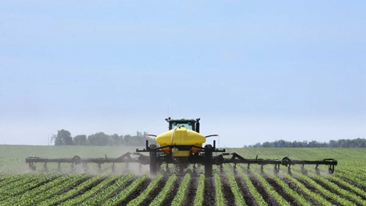 Tractor using a row-crop fertilizer applicator across a planted field.