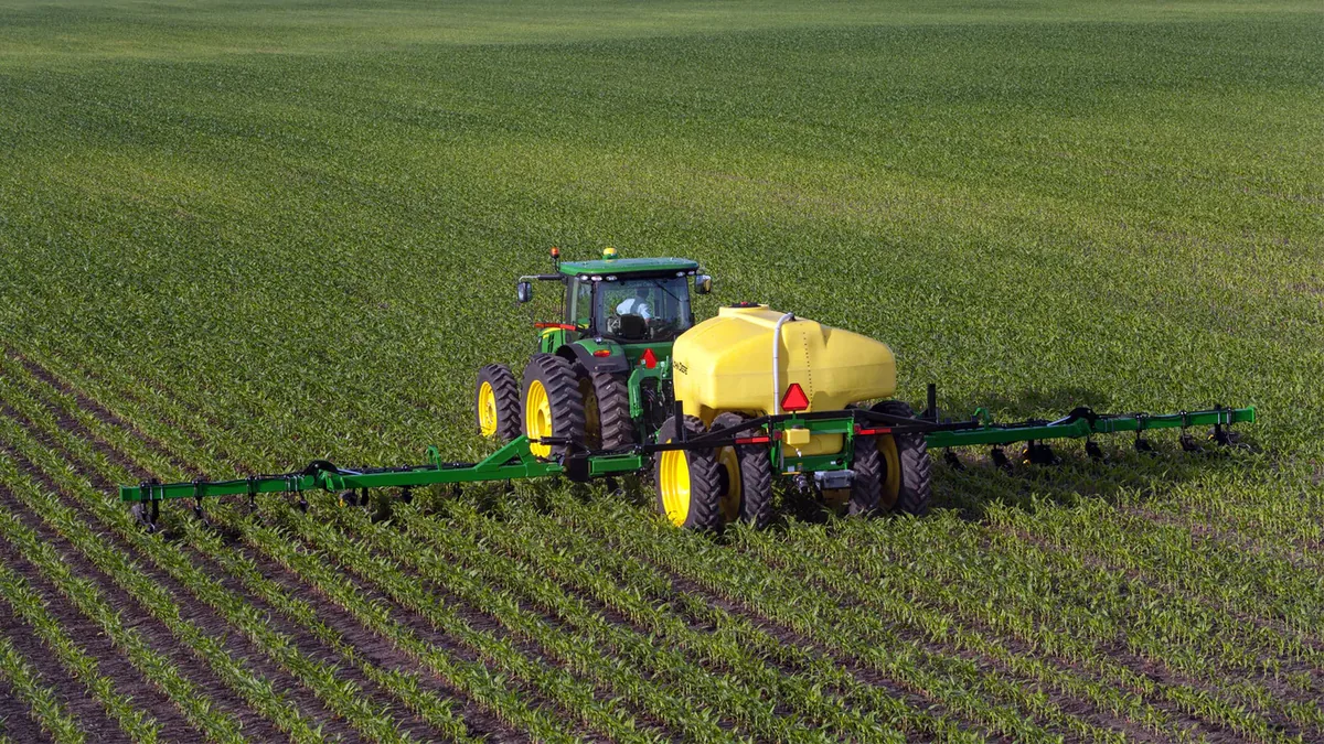 Tractor using a row-crop fertilizer applicator across a planted field.
