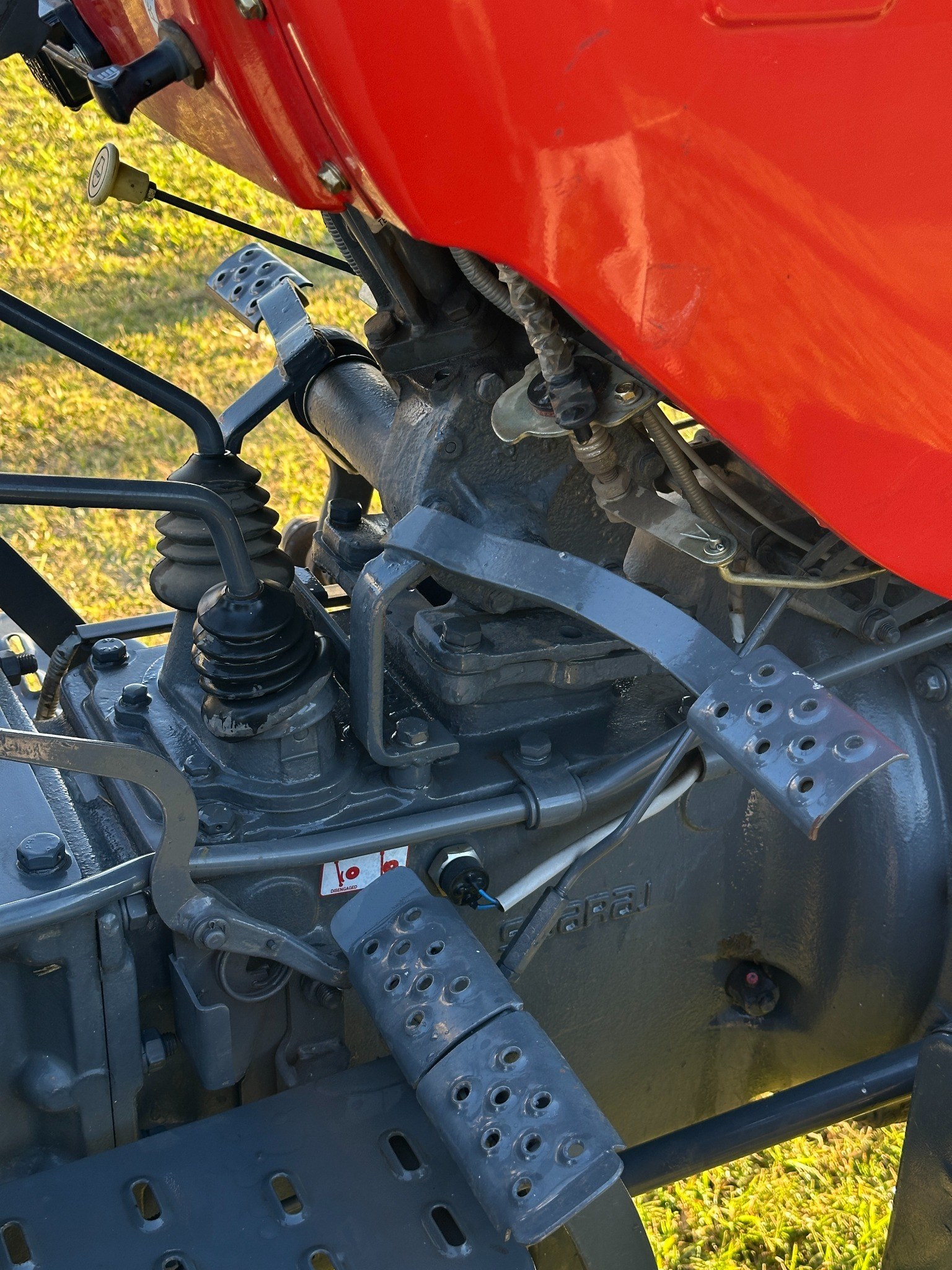 Close-up of a red tractor’s transmission, gear levers, pedals, and mechanical controls.